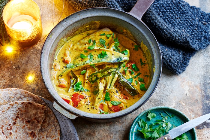 A serving bowl of yellow mackerel curry with tomatoes and coriander