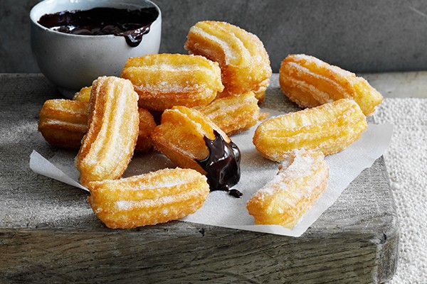 A handful of small churros next to a pot of hot chocolate dipping sauce