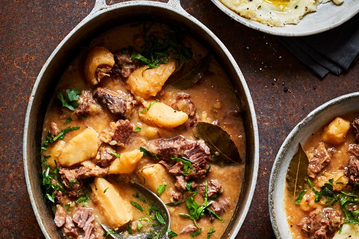 An oval casserole dish filled with a slow cooked beef and parsnip stew with a side of mashed potato