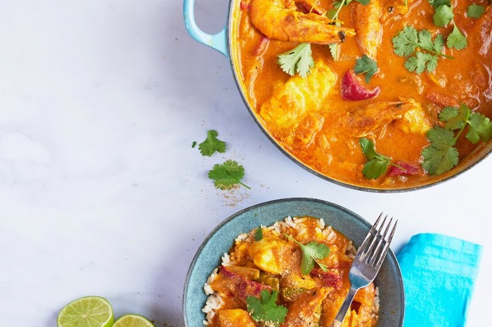 A casserole pot filled with Brazilian moqueca containing large prawns next to a plate filled with a portion