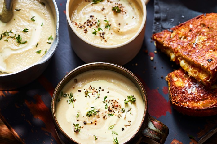 Two mugs filled with white celeriac soup with a golden grilled cheese sandwich on the side