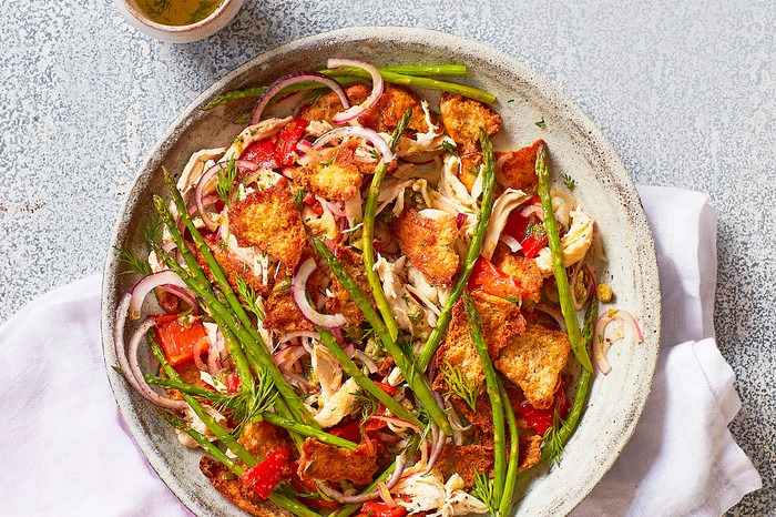 A plate of chicken, asparagus and red peppers on a white cloth with a speckled grey background