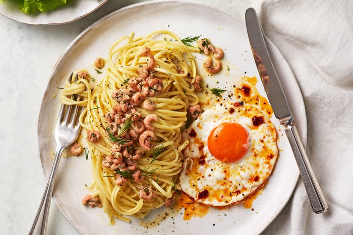 Plate of linguine topped with potted prawns and dill, next to a fried egg with chilli crisp