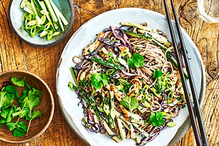 A sesame and chicken noodle salad with chopsticks and sides of spring onion and herbs