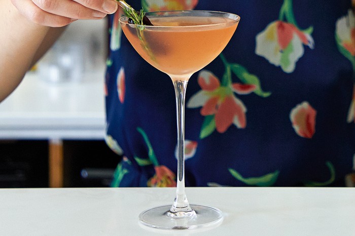 A woman adding a thyme garnish to an orange cocktail