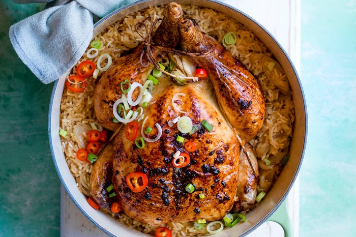 A whole roast chicken in a pot on a turquoise table