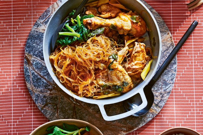 A metal pot filled with roast chicken, glass noodles and leafy green vegetables