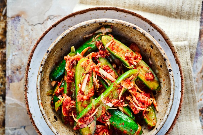 Cucumber Kimchi sliced in half with kimchi sprinkled on top, served in a deep speckled blue and grey bowl