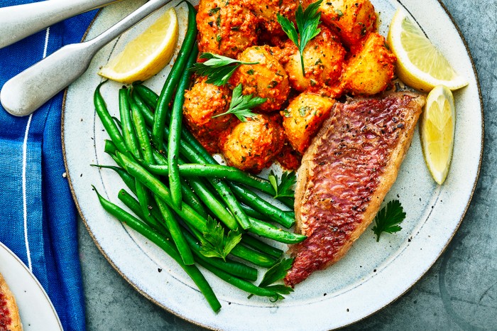 A grey plate topped with pan-fried fish, golden potatoes, green beans and slices of yellow lemons