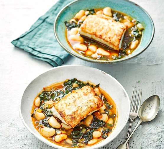 Two plates of pan fried cod, served with giant butter beans and chard, next to a fork and spoon.