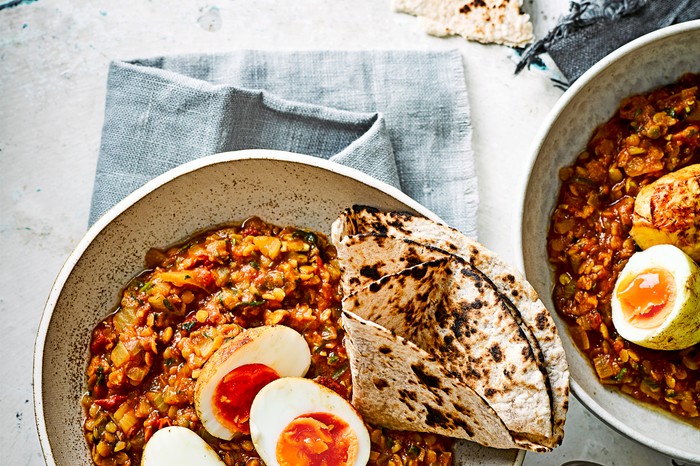Two bowls of red lentil curry with crispy eggs and a paratha