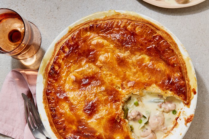 A golden-crusted pie with a creamy chicken filling in a pie dish, with a pink napkin and cutlery