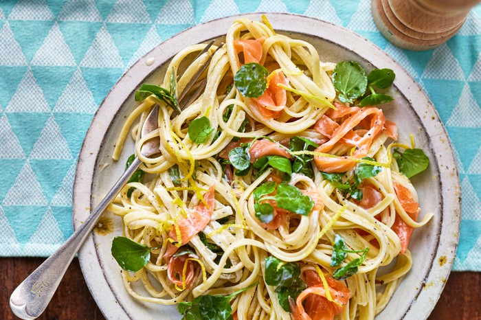 A plate of linguine with smoked salmon and watercress in, on a turquoise tablecloth