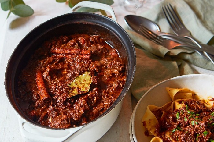 An ovenproof pot filled with stifado stew, next to a bowl of pasta with the stew piled on top