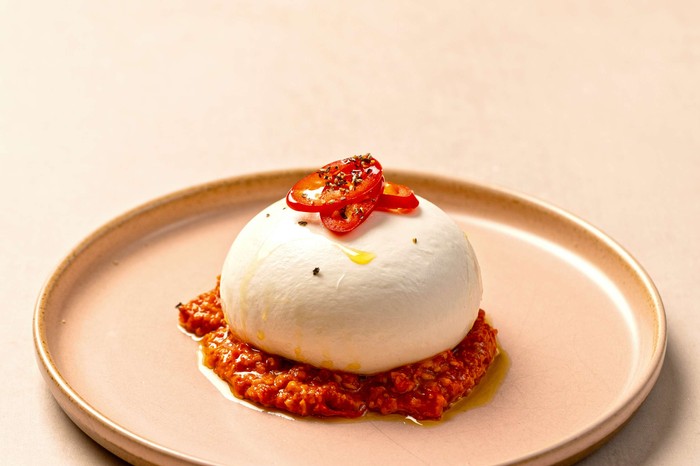 A whole burrata ball on a small serving plate with romesco pepper underneath it and on top