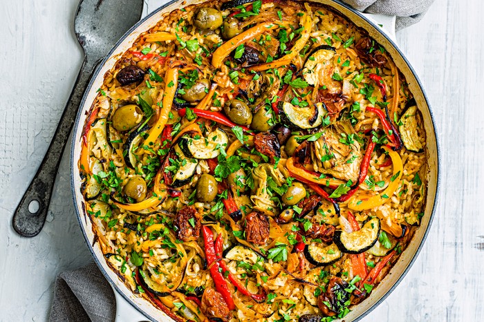 A large pot of vegan paella with sun blush tomatoes, olives, peppers and courgettes