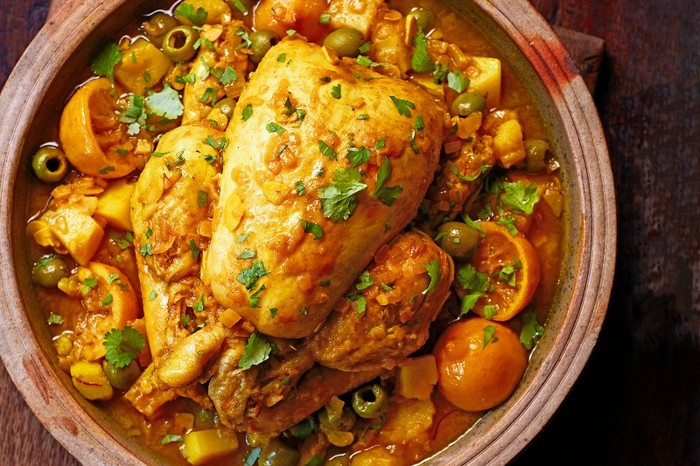 Chicken in a pot surrounded by vegetables an topped with herbs
