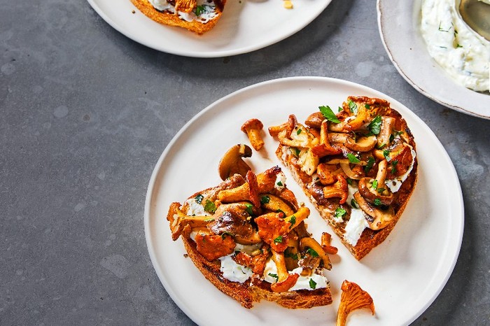 A white plate of wild mushrooms and horseradish labneh on toast on a grey background